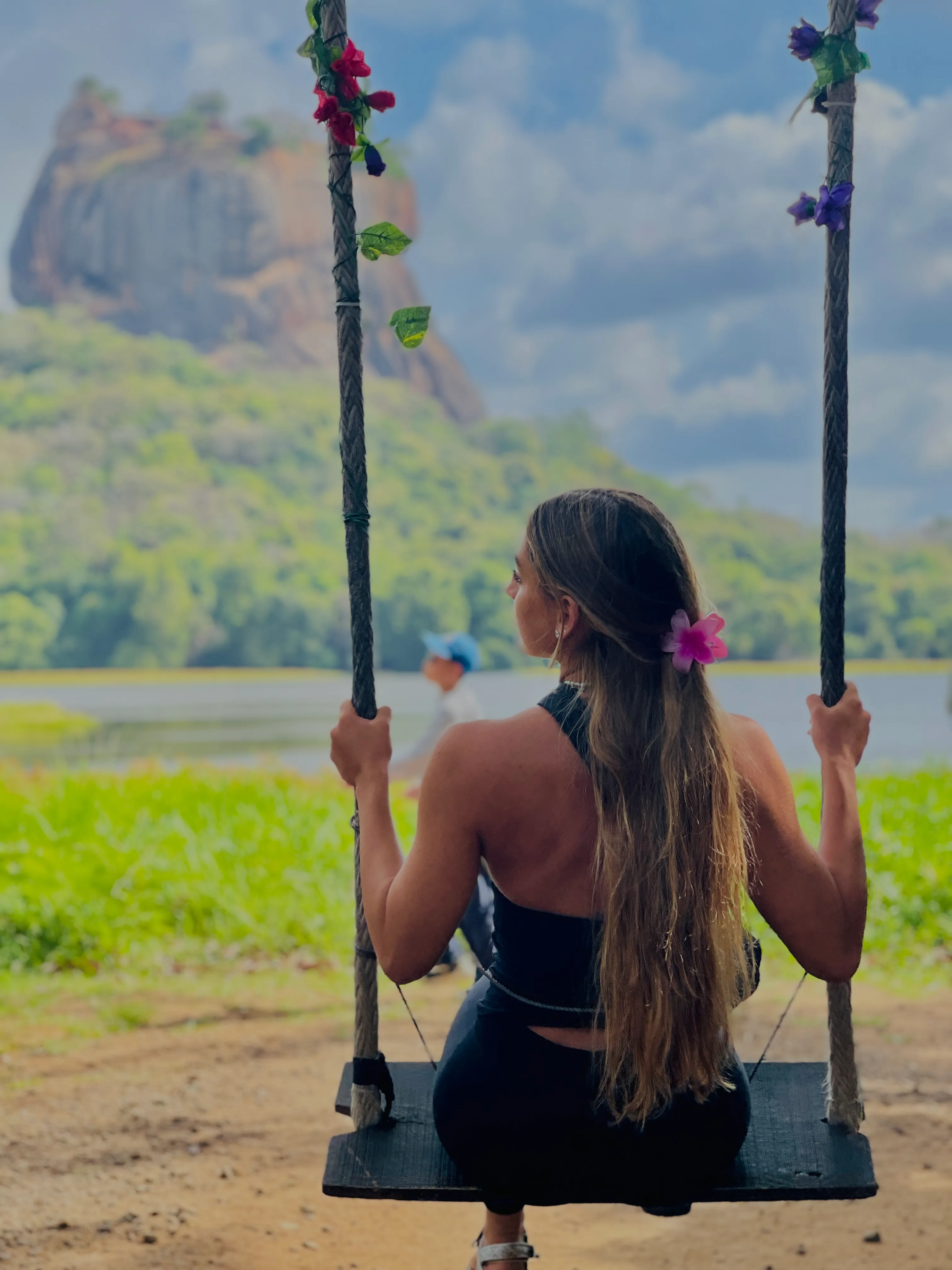 A guest on a flower-decked rope swing, looking out across the lake to Sigiriya rock
