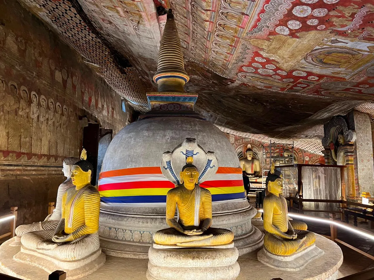 Seated Buddha statues around a stupa beneath the painted ceiling of a Dambulla cave shrine