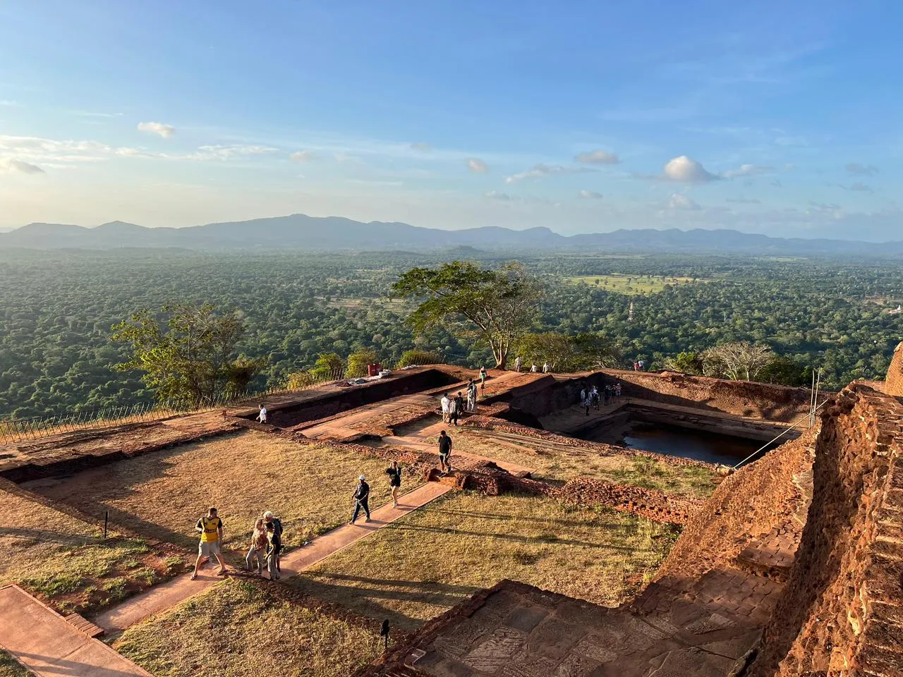 Visitors walking the brick foundations and rock-cut pool of the summit palace on Sigiriya
